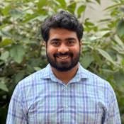 Bharat Savaram, Power BI specialist, wears a plaid button up in his headshot and stands in front of a tree